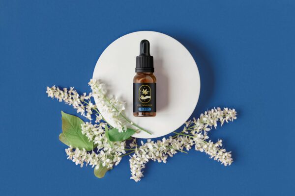 Amber glass dropper cosmetic bottle on oval podium, red orange background. Natural skin care, SPA design. Mineral organic oil. Product Mock-Up. Oily pipette. Flat lay, Top View. White flowers